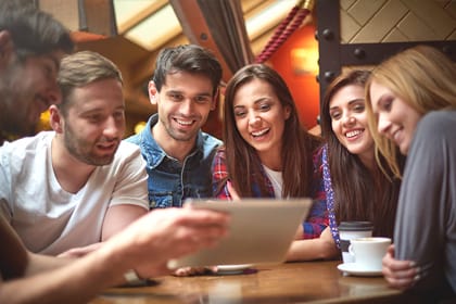 "Grupo de jóvenes en una cafetería disfrutando de un curso de comunicación y oratoria, aprendiendo juntos con contenido digital.